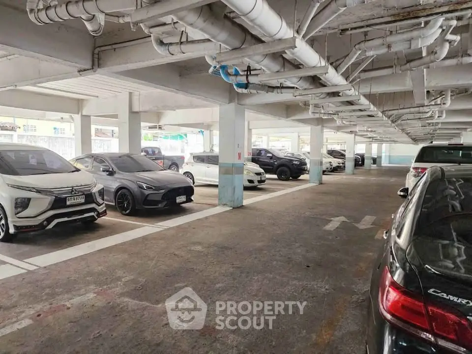 Spacious indoor parking area with multiple vehicles and overhead piping.