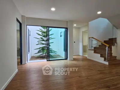 Spacious modern living room with wooden flooring and large glass doors opening to a small courtyard.