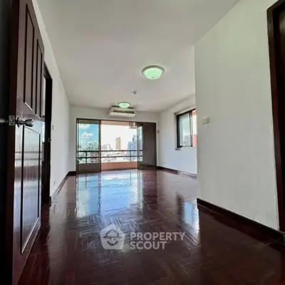 Spacious living room with wooden flooring and city view balcony in modern apartment.