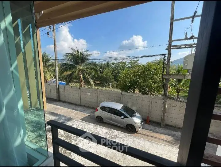Scenic view from balcony overlooking tropical landscape and parked car on quiet street.