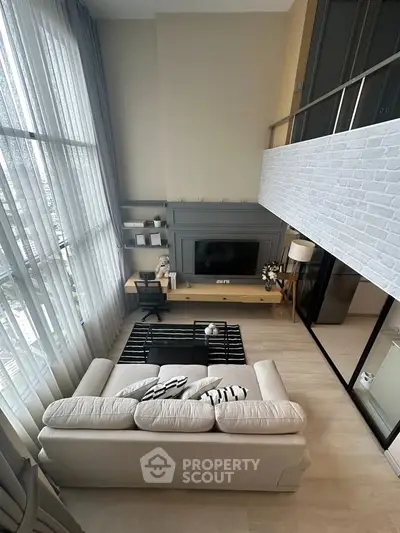 Modern loft-style living room with high ceilings and large windows, featuring a cozy sofa and sleek entertainment setup.