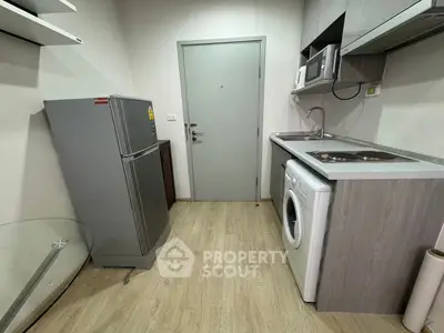 Compact kitchen with modern appliances including fridge, washing machine, and microwave in a cozy apartment.