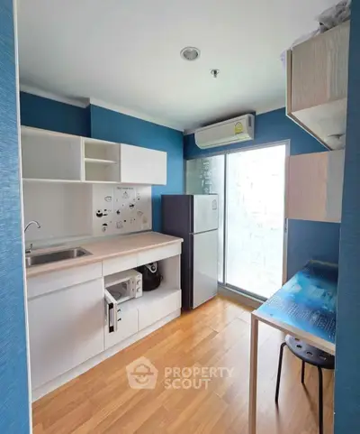 Modern kitchen with sleek cabinetry and natural light, featuring a refrigerator and air conditioning unit.