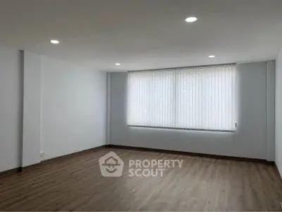 Spacious empty room with wooden flooring and large window, perfect for customization.