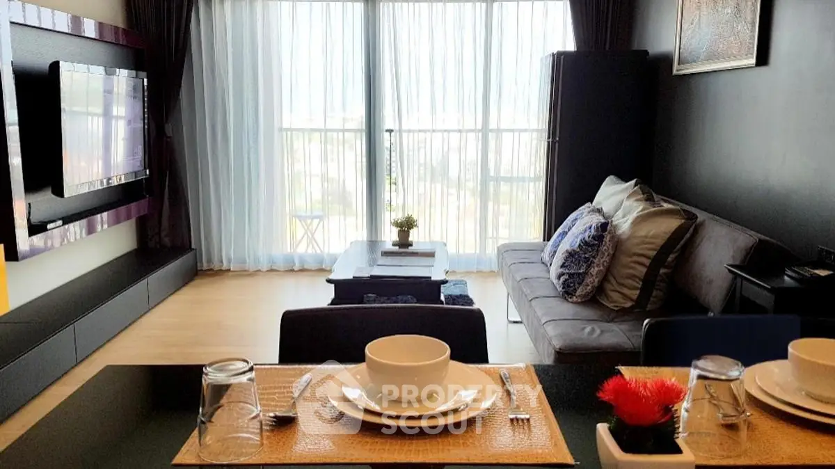 Modern living room with large TV, cozy sofa, and dining setup in a bright apartment.