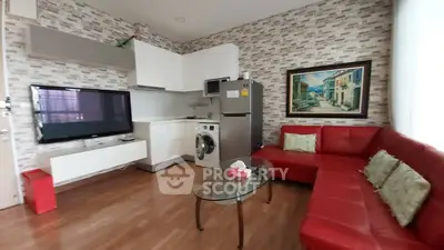 Modern living room with red sofa, wall-mounted TV, and compact kitchen area featuring washing machine and fridge.