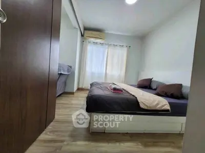 Cozy bedroom with wooden flooring and natural light, featuring a comfortable bed and air conditioning.