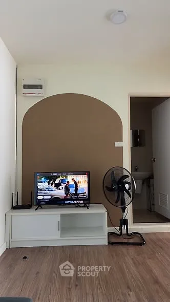 Modern living room with TV, fan, and wooden flooring in cozy apartment.