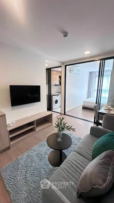 Modern living room with open layout, featuring a cozy sofa, wall-mounted TV, and view into a stylish bedroom.