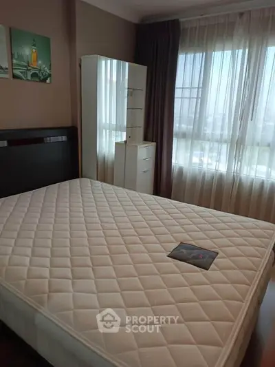 Spacious bedroom with large window and modern decor in a high-rise apartment.