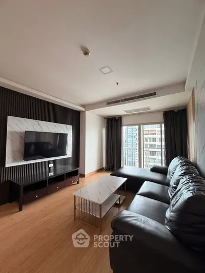 Modern living room with sleek black sofa, wall-mounted TV, and city view from large window.
