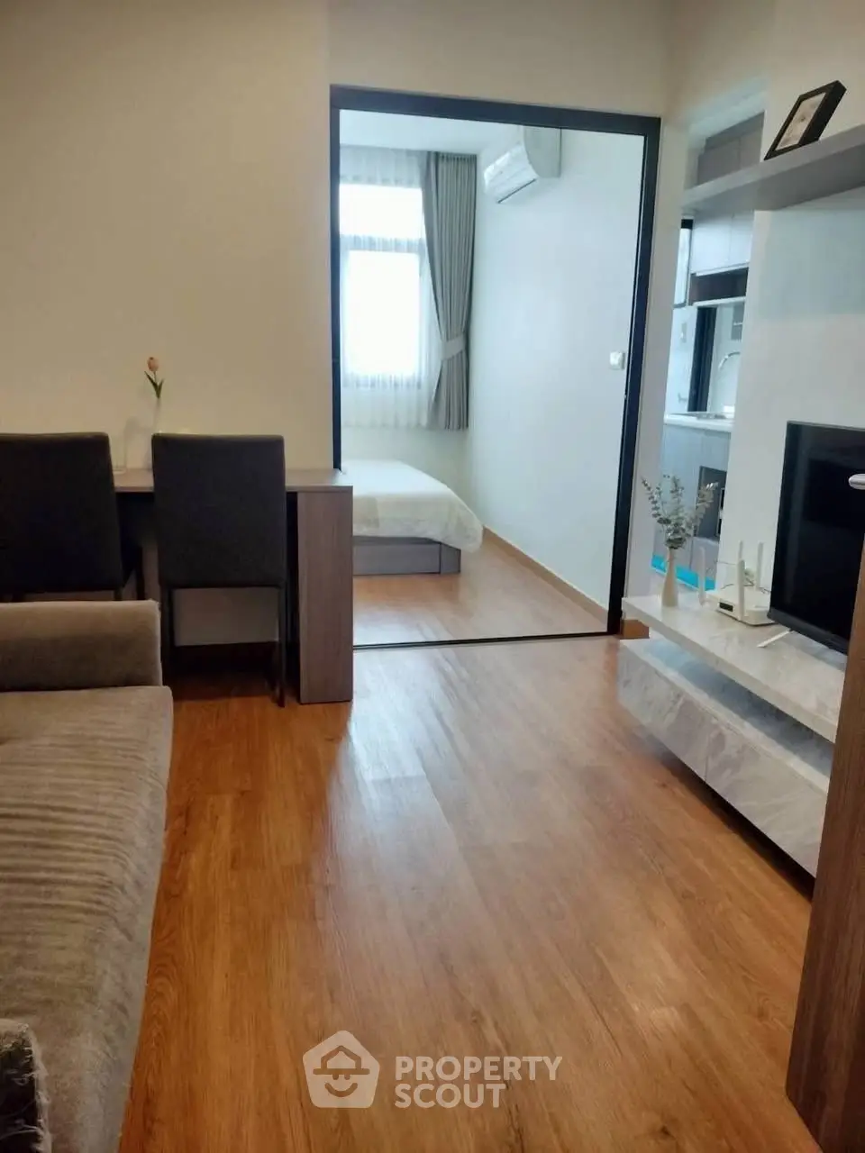 Modern apartment with open living room and bedroom, featuring sleek wooden flooring.