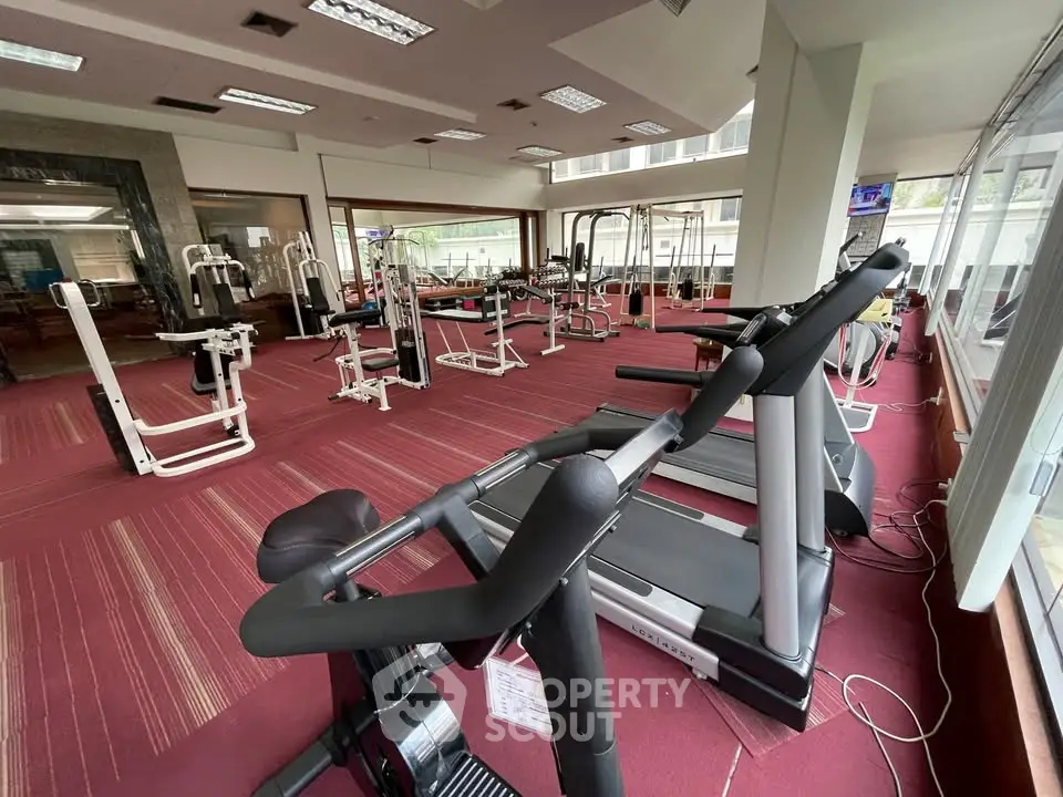 Spacious gym with modern fitness equipment and large windows for natural light.