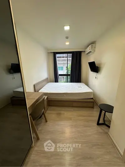 Modern bedroom with large window and minimalist furnishings in urban apartment.