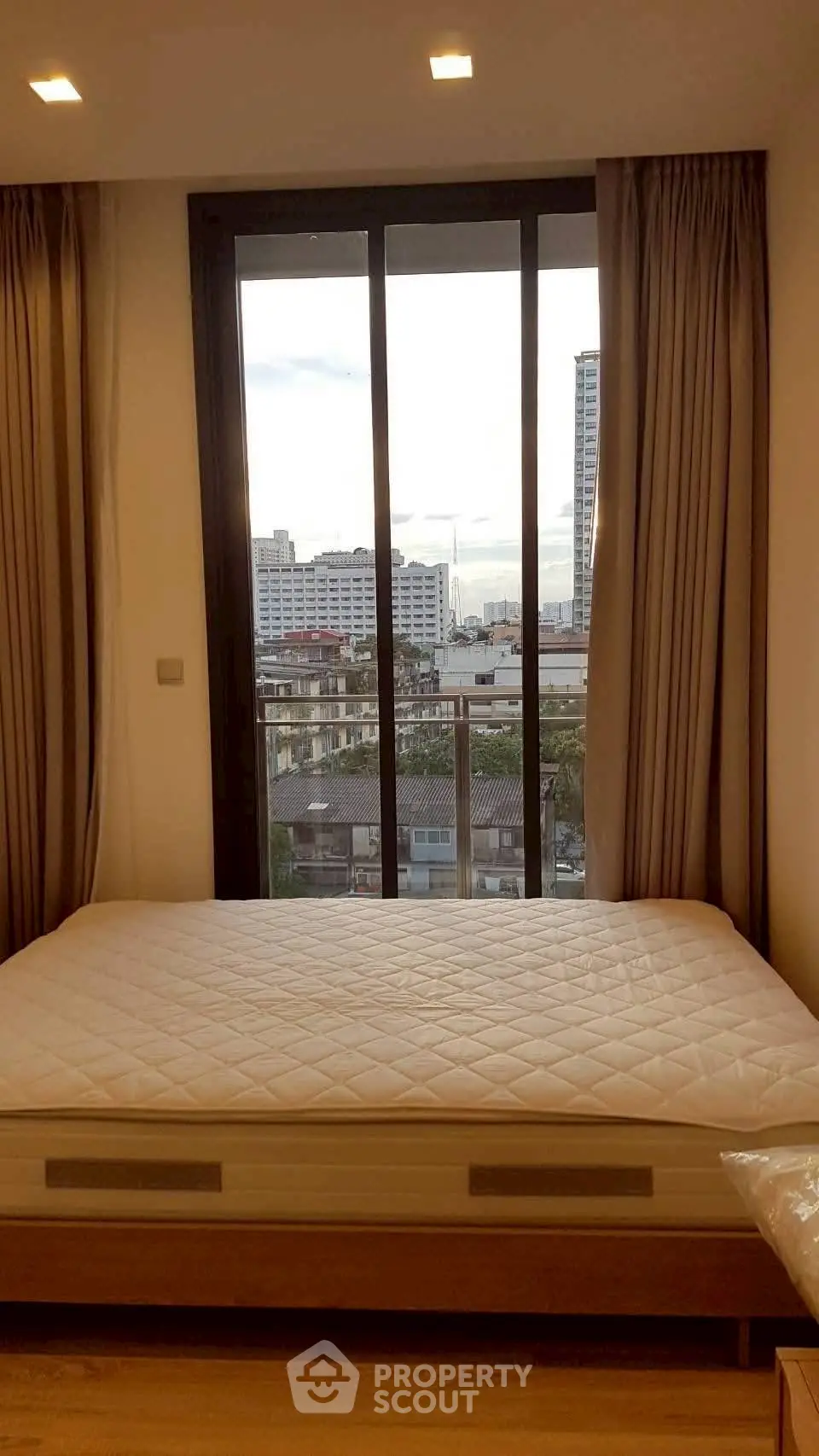 Cozy bedroom with large window offering city view, featuring a comfortable bed and elegant curtains.