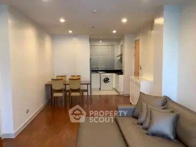Modern open-plan living room with kitchen and dining area, featuring sleek furniture and hardwood floors.