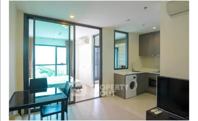 Modern apartment interior with open kitchen and living area, featuring a washing machine and large windows.