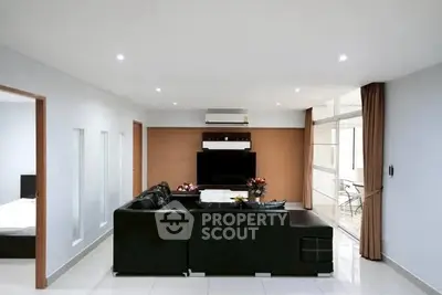 Spacious modern living room with sleek black sofa and large TV, ideal for entertainment.