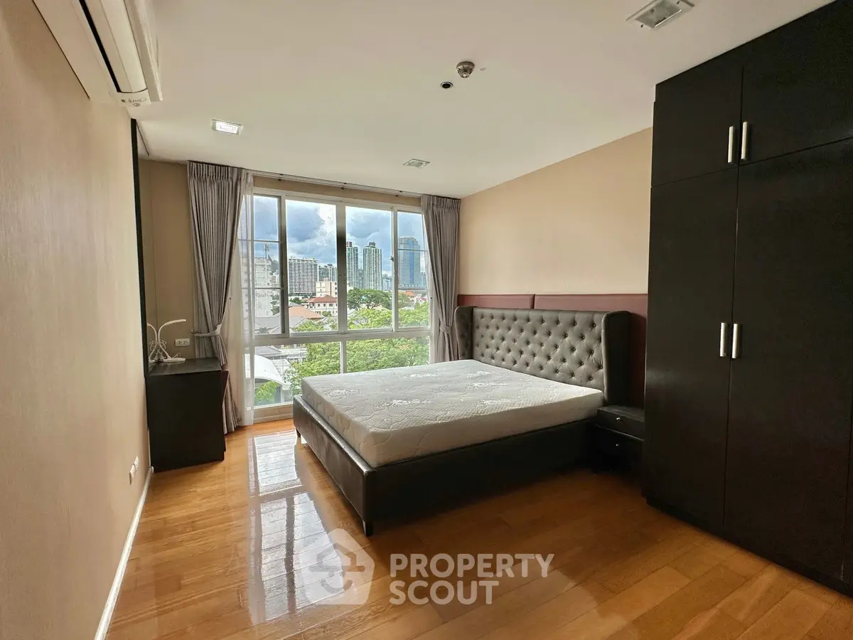 Spacious bedroom with city view and modern furnishings in a high-rise apartment.