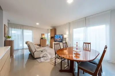Spacious living room with elegant dining area and modern furniture, featuring large windows for natural light.
