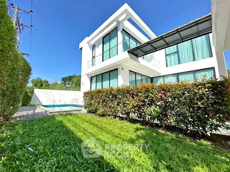 Modern two-story house with lush garden and private pool under clear blue sky.