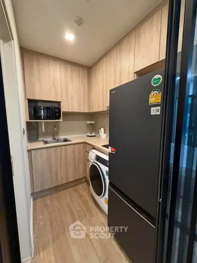 Modern kitchen with wooden cabinets, sleek appliances, and washing machine in compact layout.
