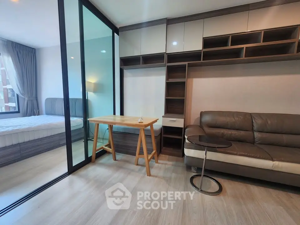 Modern apartment interior with cozy living room and stylish bedroom separated by glass partition.