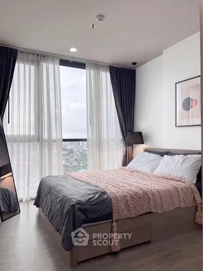 Modern bedroom with large windows and city view, featuring stylish decor and cozy bedding.