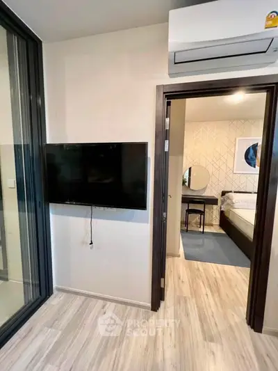 Modern apartment interior with wall-mounted TV and air conditioning, leading to a cozy bedroom.