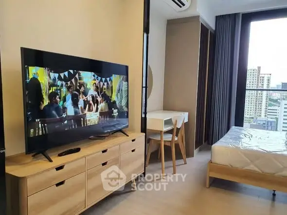 Modern studio apartment with TV, bed, and city view balcony.