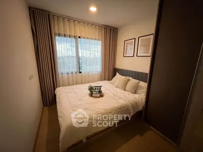 Cozy bedroom with modern decor and large window offering natural light and city view.