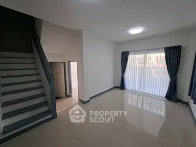 Spacious modern living room with large window and staircase, perfect for family gatherings.