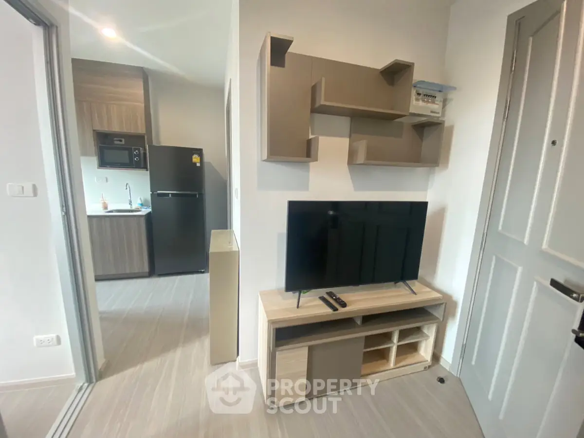 Modern apartment interior with sleek kitchen and cozy living area featuring a flat-screen TV and stylish shelving.