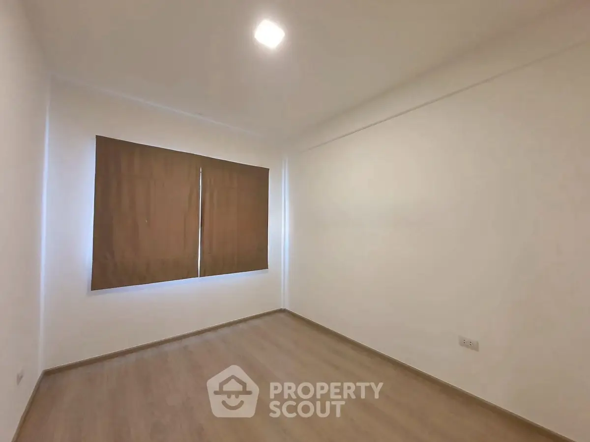 Spacious empty room with wooden flooring and large window, perfect for customization.