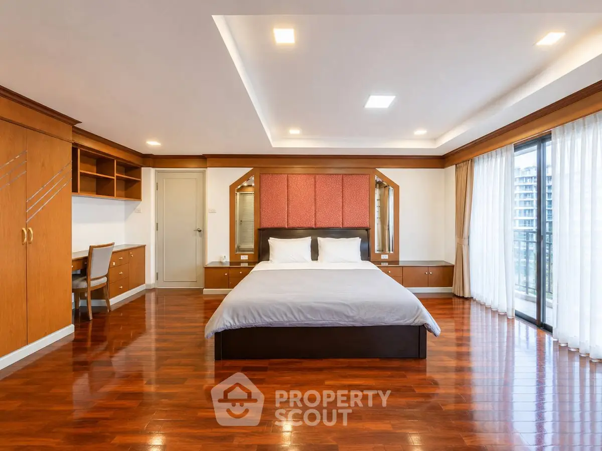 Spacious bedroom with elegant wooden flooring and large windows offering natural light.