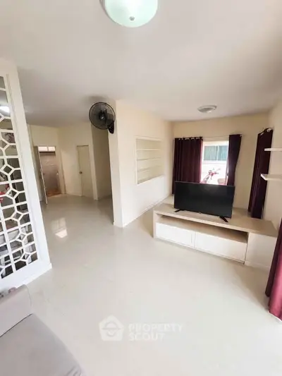 Spacious living room with modern decor and natural light, featuring a sleek TV unit and elegant curtains.
