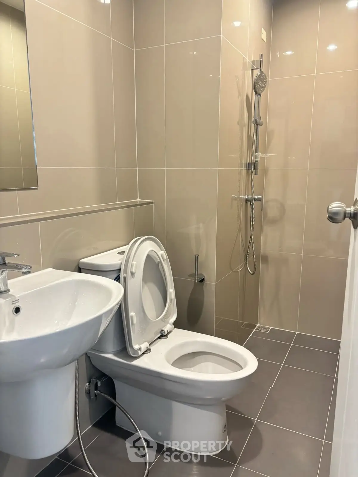 Modern bathroom with sleek fixtures and neutral tiles, featuring a shower and toilet.