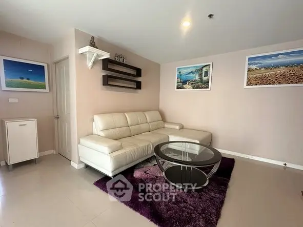 Modern living room with white leather sofa, glass coffee table, and vibrant wall art.