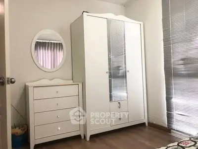 Cozy bedroom with white wardrobe and dresser, featuring a round mirror and blinds.