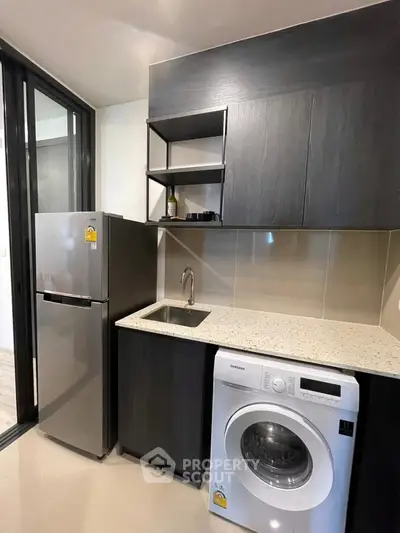 Modern kitchen with sleek cabinets, washing machine, and compact fridge in stylish apartment.