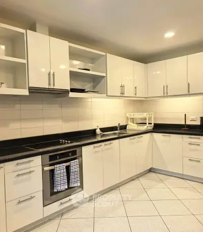 Modern kitchen with sleek white cabinets and black countertops, featuring built-in oven and electric stove.