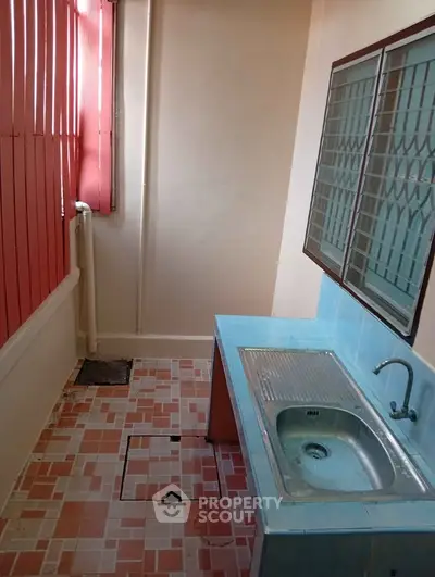 Compact kitchen area with tiled floor and stainless steel sink, featuring large windows for natural light.