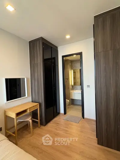 Modern bedroom with ensuite bathroom and wooden flooring, featuring sleek black wardrobes and a compact study desk.