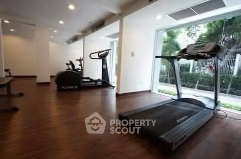 Spacious gym with modern equipment and large windows overlooking greenery.