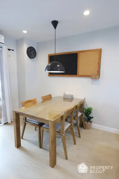 Modern dining area with wooden table and chairs, pendant light, and wall clock