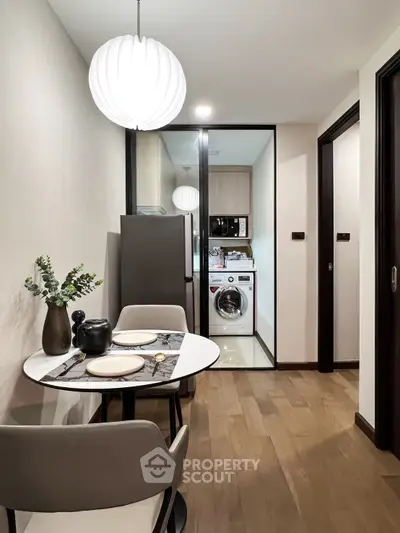 Modern dining area with view into compact kitchen featuring washing machine and microwave.