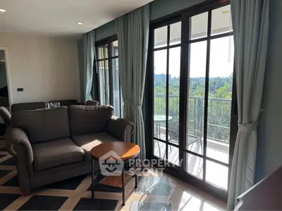 Spacious living room with large windows and balcony offering stunning views of lush greenery.