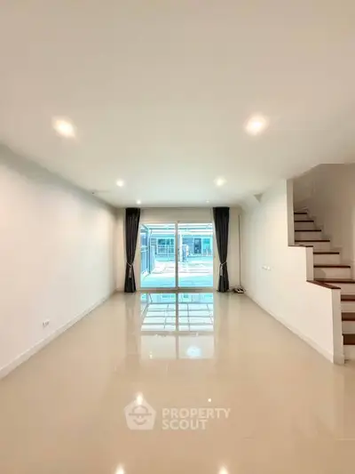 Spacious living room with glossy floors and large sliding glass doors leading to a bright outdoor area.