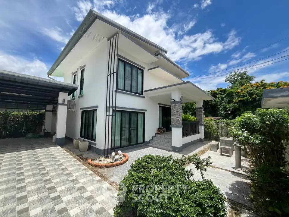 Modern two-story house with spacious driveway and lush greenery under a clear blue sky.
