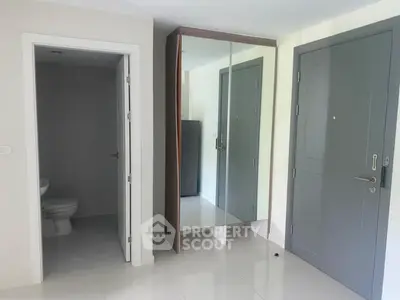 Modern apartment entrance with sleek mirrored closet and adjacent bathroom.